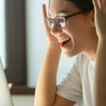 Female student with her hands up looking excited at her laptop